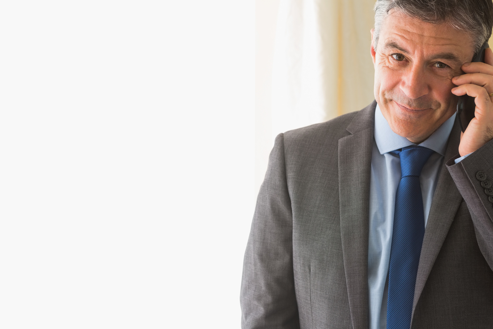 Amused mature businessman calling someone with his mobile phone on white background