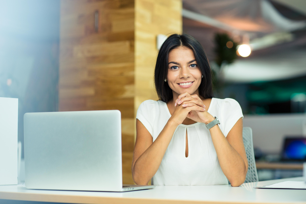 Portrait of a cheerful businesswoman sitting at the table in office and looking at camera